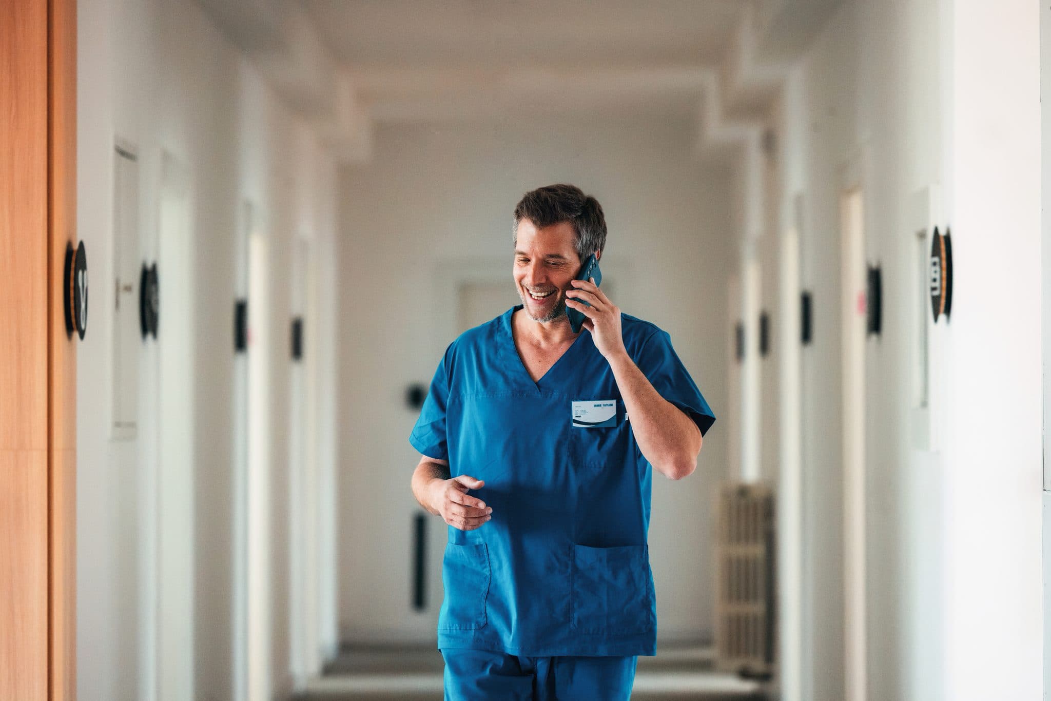 Pfleger telefoniert im Gehen auf einem hellen Stationsflur