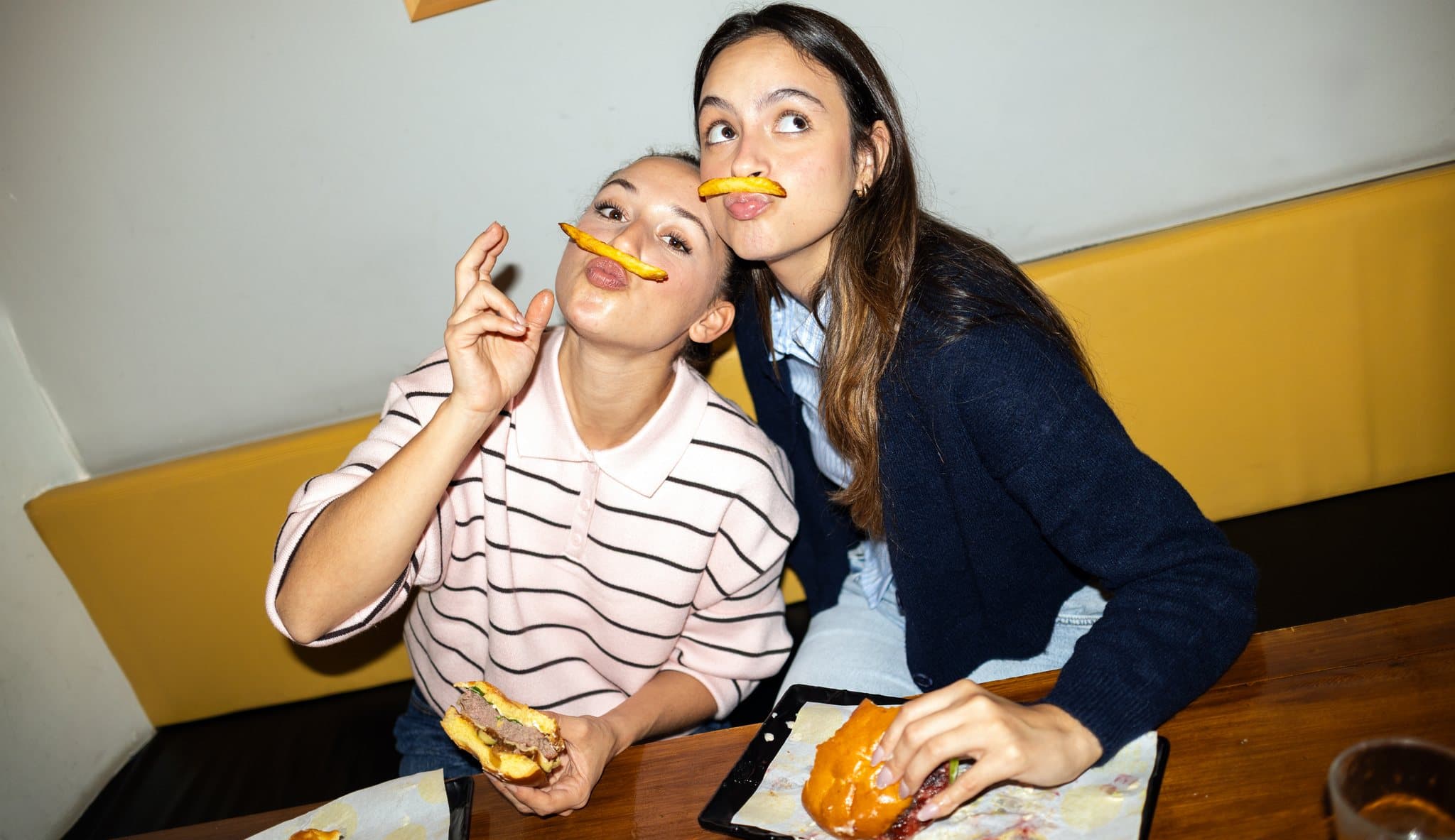 Zwei Freundinnen sitzen lachend in einem Diner, Pommes in der Hand