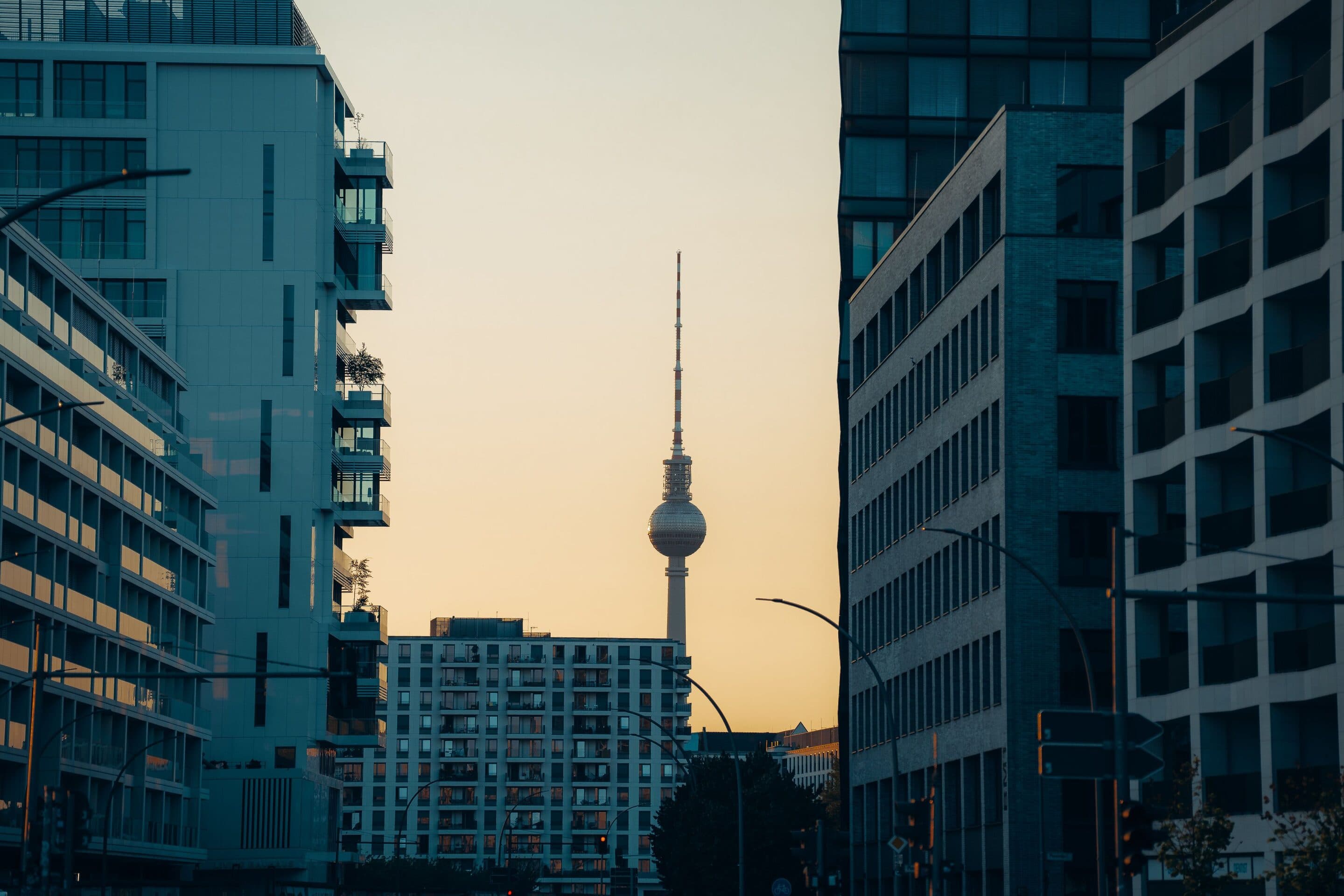 Der Berliner Fernsehturm mit Kugel und Antennenspitze, zu sehen zwischen Wohn- und Bürogebäuden bei Sonnenuntergang