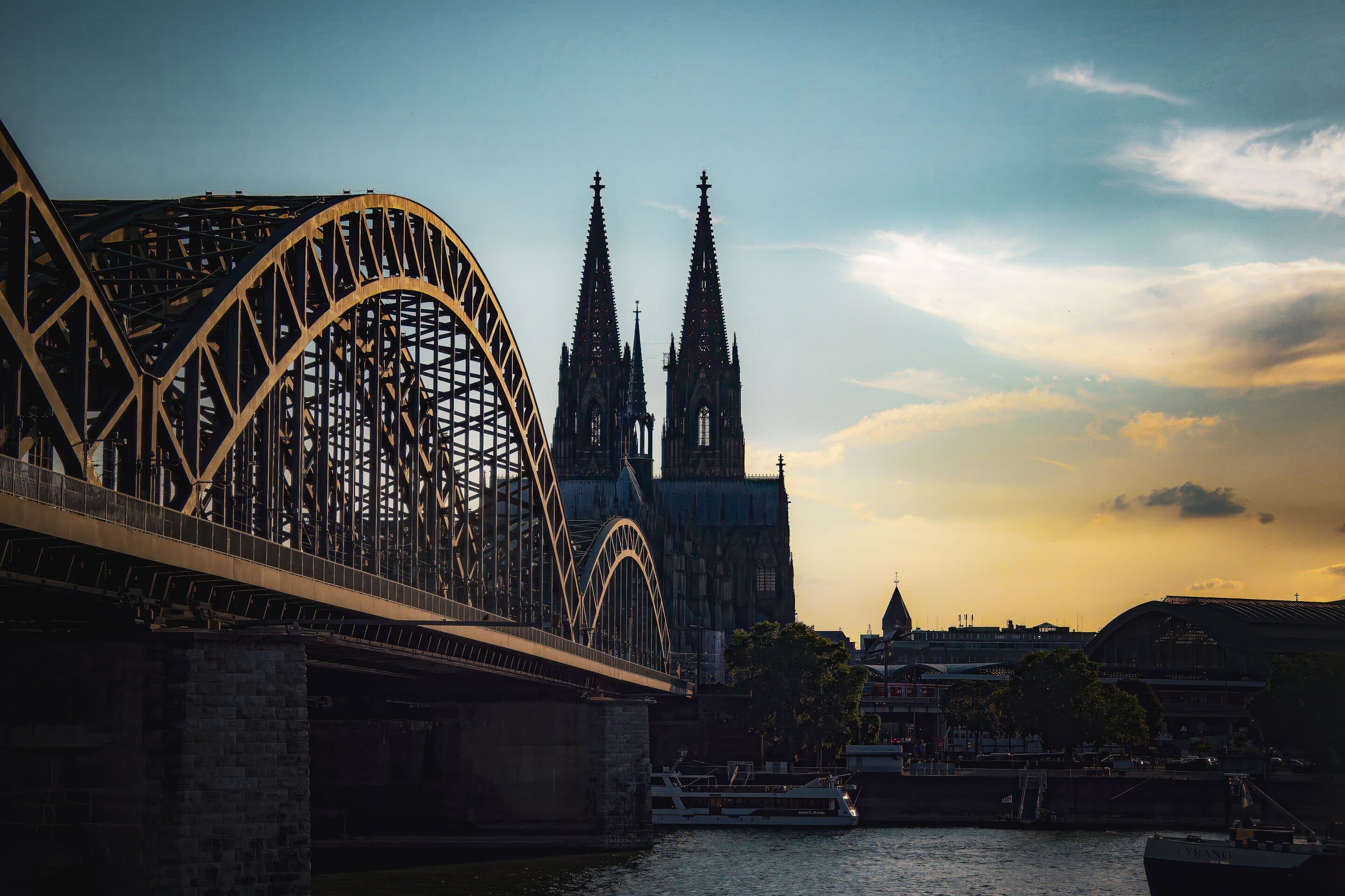 Die Kölner Hohenzollernbrücke im Vordergrund, dahinter die Türme des Kölner Doms bei Sonnenuntergang