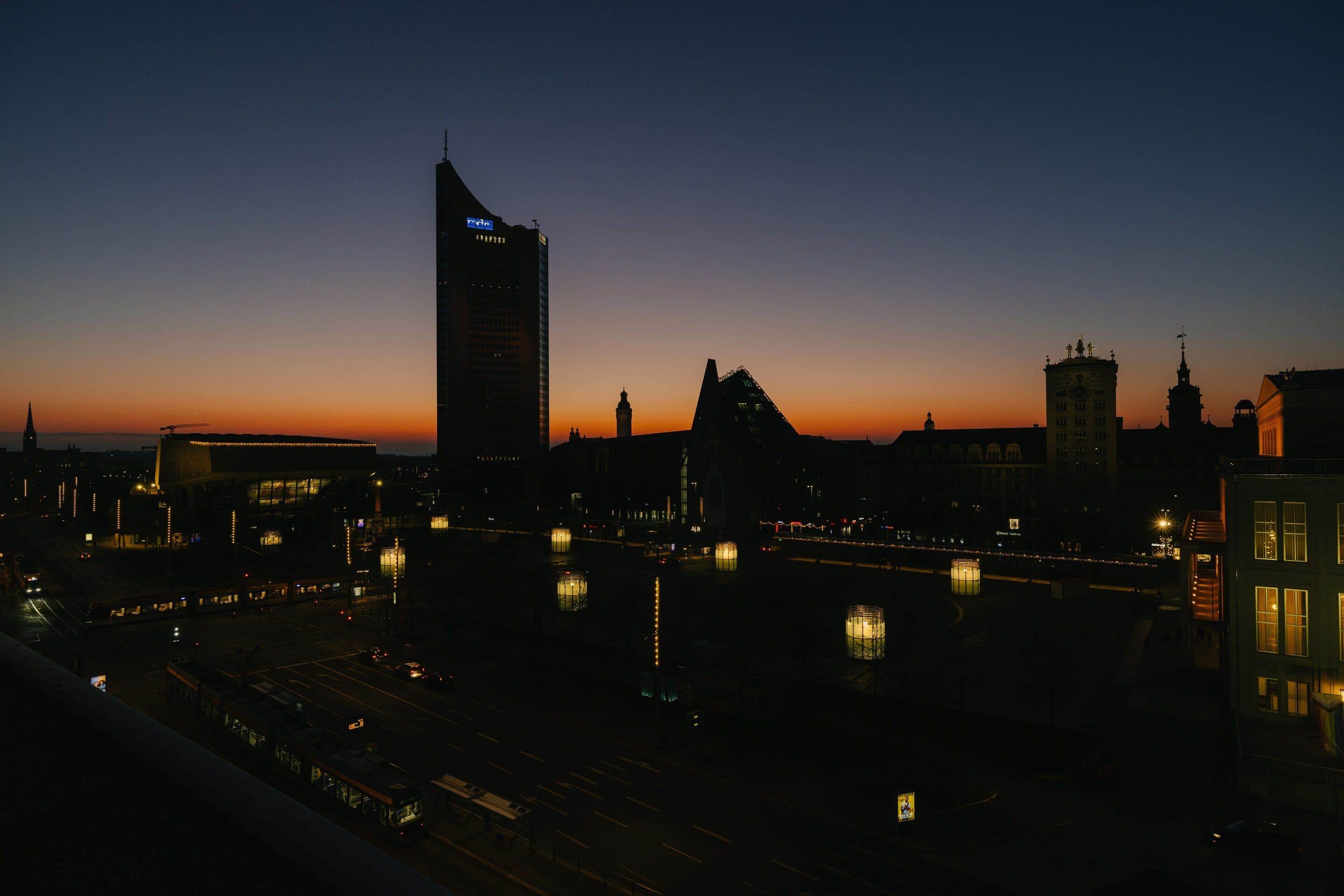 Leipzigs Skyline bei Sonnenuntergang mit dem MDR-Turm und einem gläsernen Giebelbau am Augustusplatz