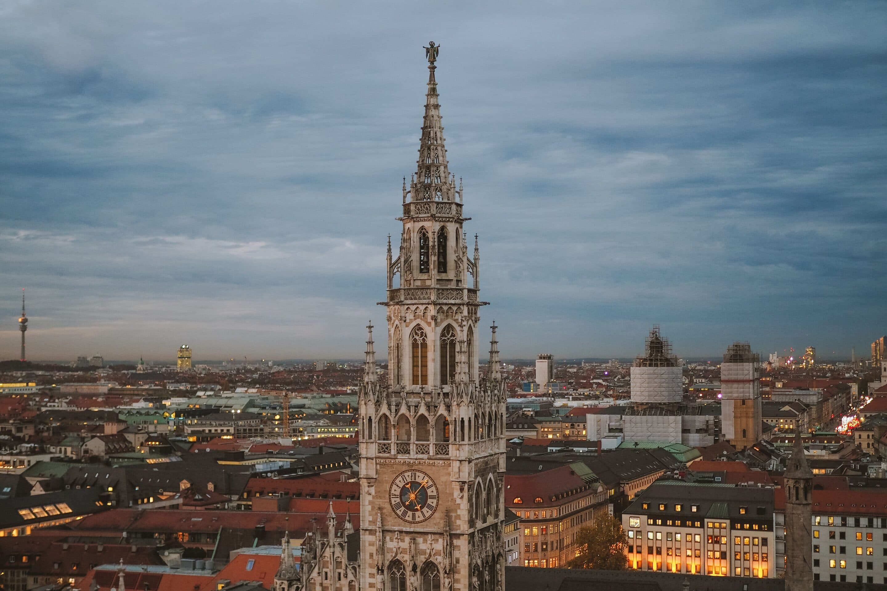Der Turm des Münchner Neuen Rathauses mit Uhr und Turmspitze, überragt die Dächer der Altstadt in der Abenddämmerung