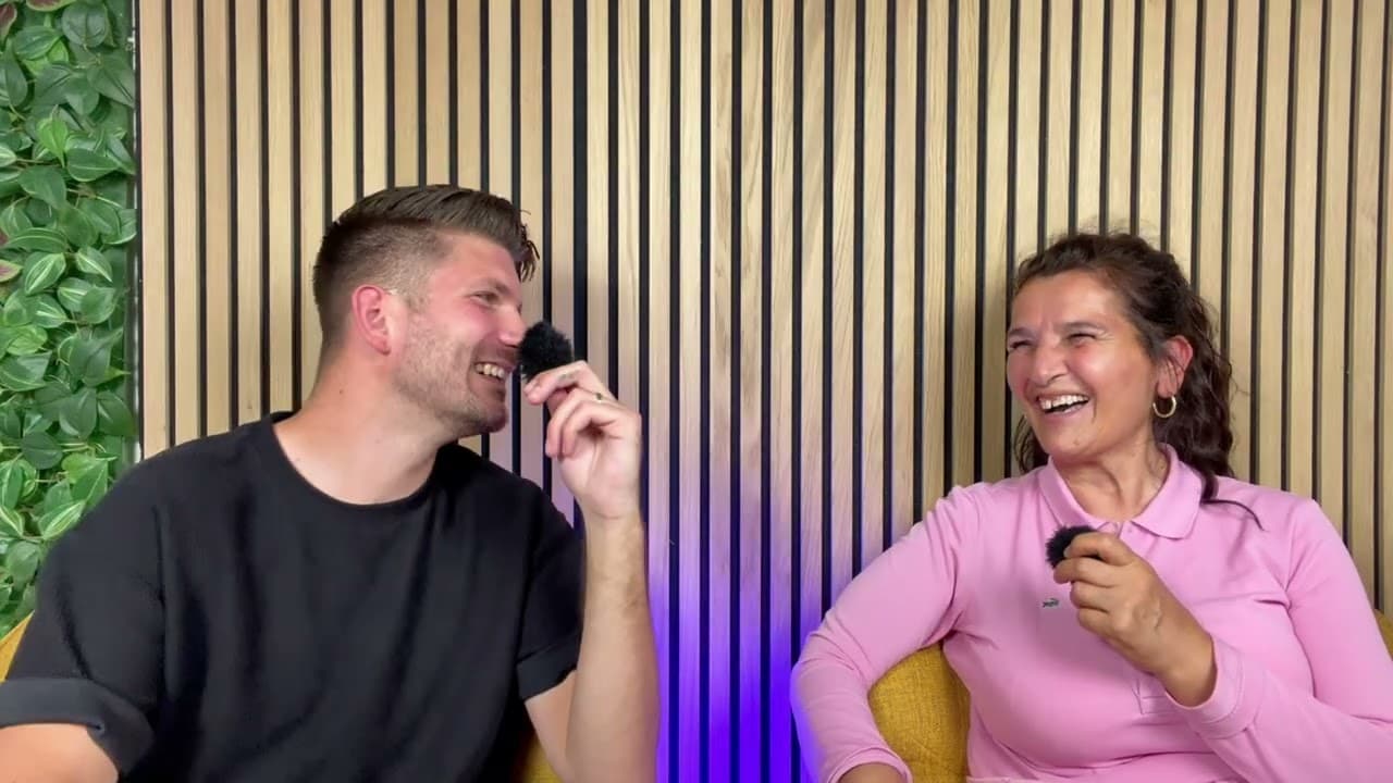 Moderator und Gesprächspartnerin lachen herzlich mit Mikrofonen vor Holzlamellenwand – überraschende Einblicke in die Zeitarbeit