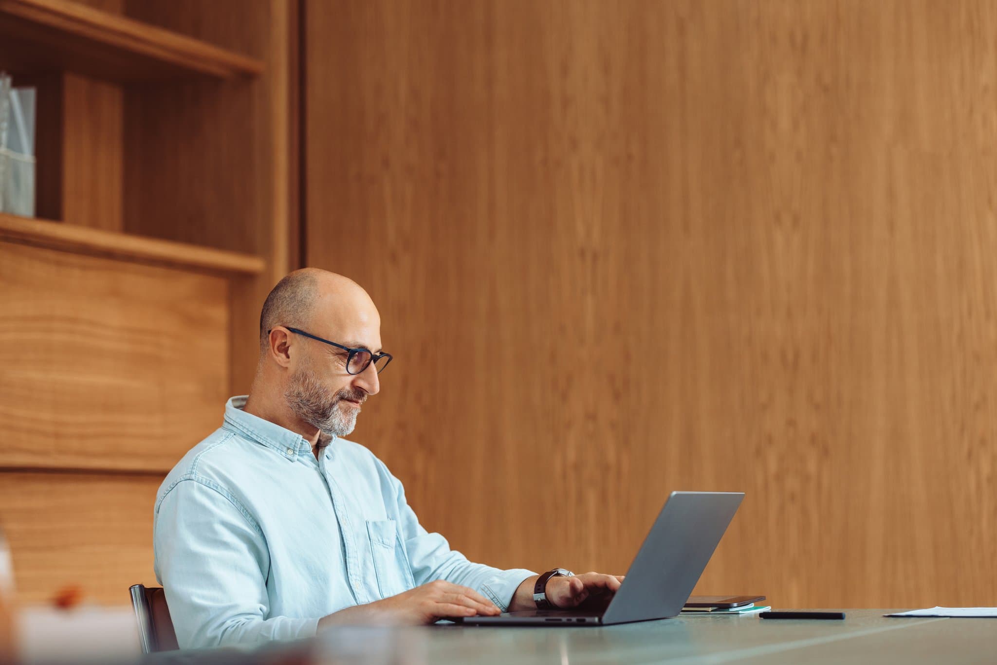 Mann arbeitet am Laptop an einem Schreibtisch vor einer Holzwand