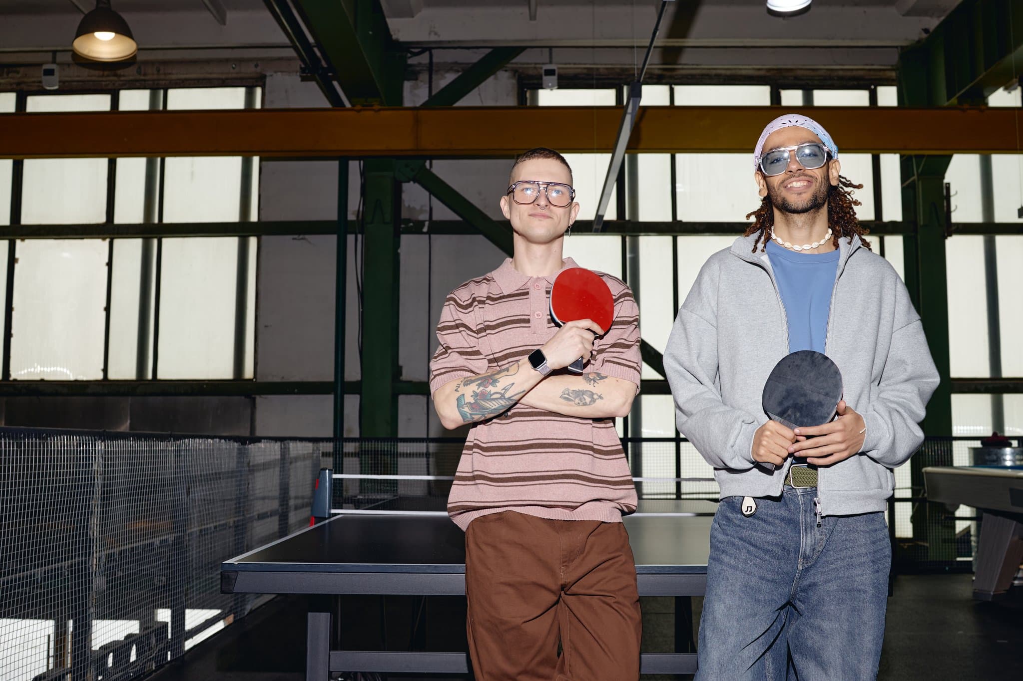Zwei Männer stehen mit Tischtennisschlägern vor einer Platte in einer Halle
