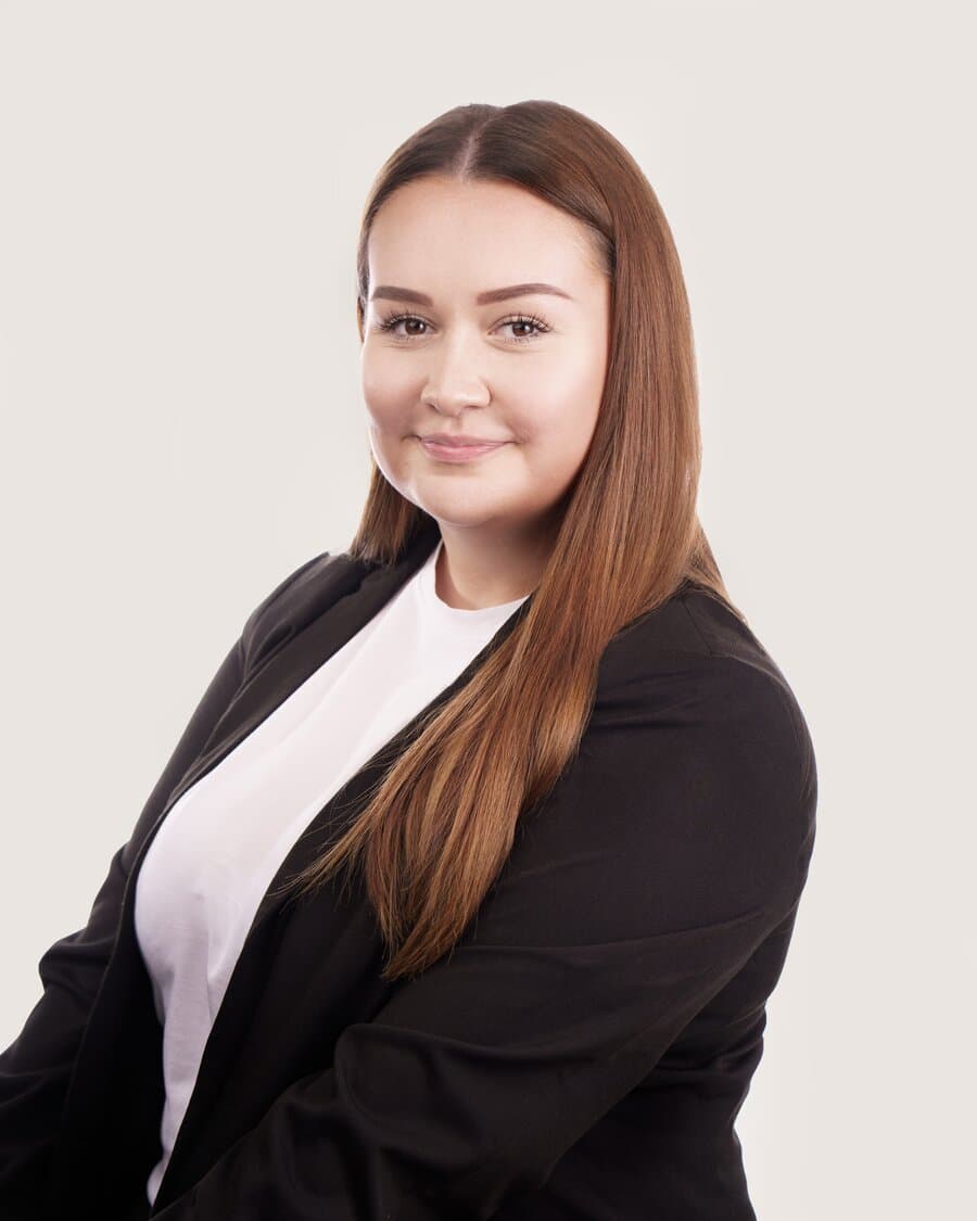 Aleksandra, Azubi in Köln, mit langem Haar und schwarzem Blazer, blickt freundlich in die Kamera