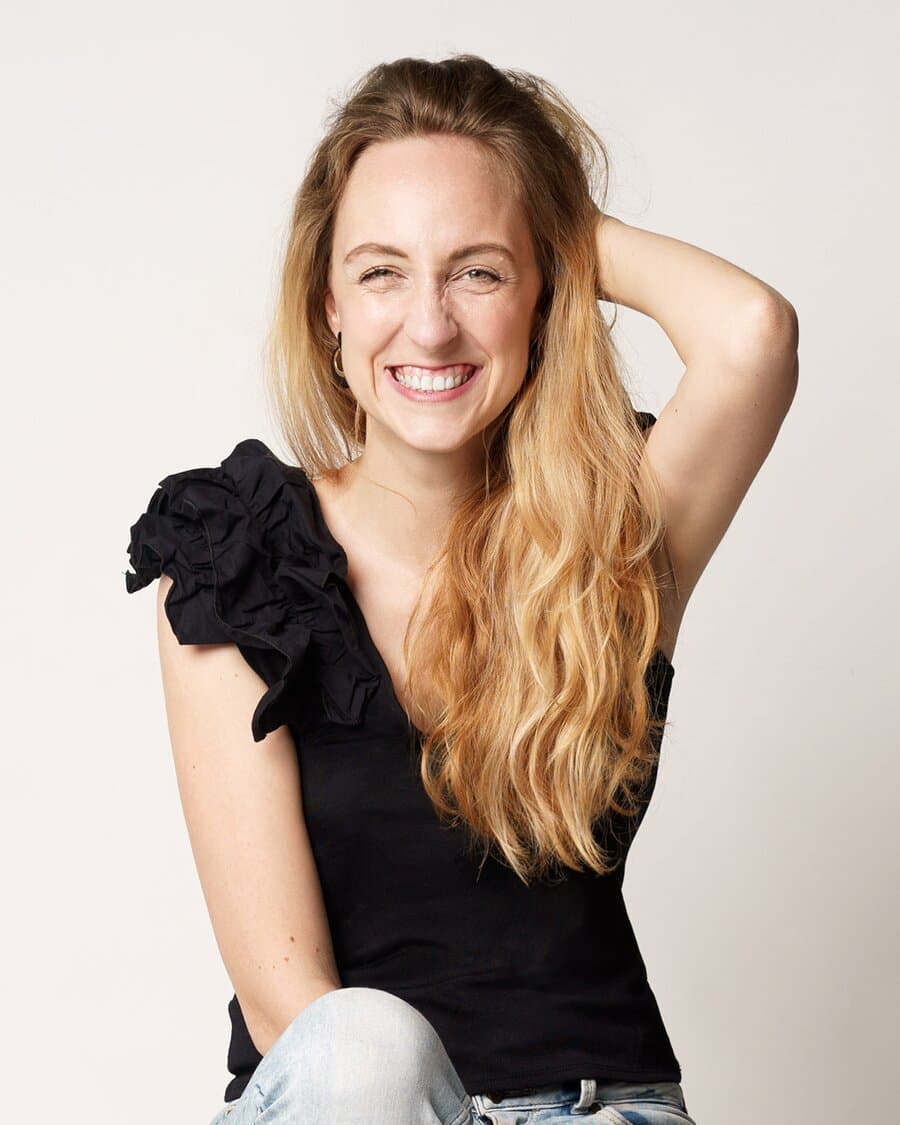 Maria, Marketing, bundesweit tätig, lacht mit langem Haar in die Kamera, eine Hand am Kopf